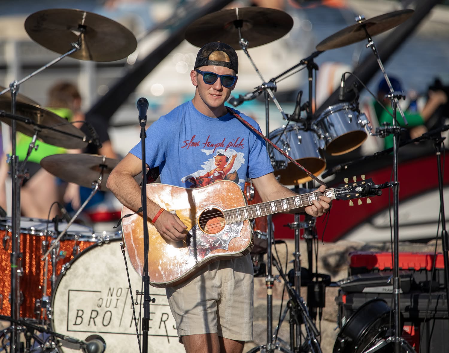 Ryan North smiling with acoustic guitar in front of a drum kit at an outdoor show